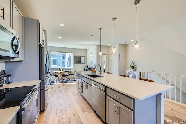 kitchen featuring stainless steel appliances, light countertops, gray cabinetry, light wood-style floors, and a sink