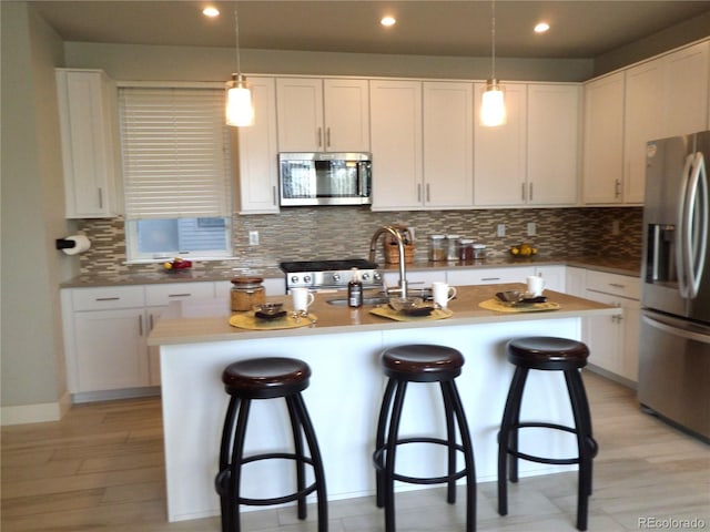 kitchen with an island with sink, hanging light fixtures, white cabinets, and stainless steel appliances