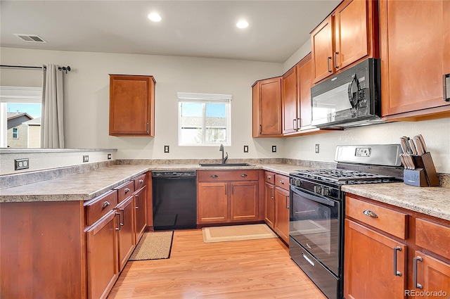 kitchen with a peninsula, light wood-style flooring, a sink, visible vents, and black appliances
