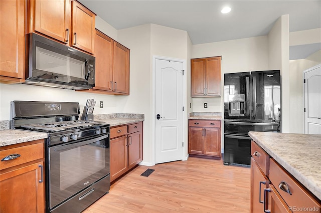 kitchen featuring brown cabinets, light countertops, visible vents, light wood-type flooring, and black appliances