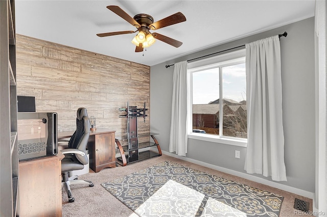 office space featuring an accent wall, carpet, wood walls, and ceiling fan