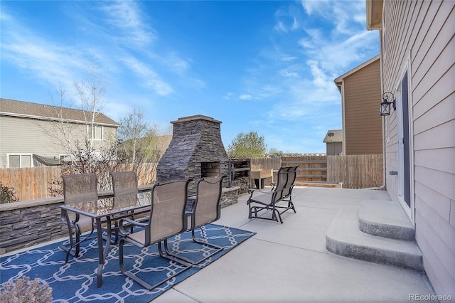 view of patio featuring outdoor dining area, fence, and an outdoor stone fireplace