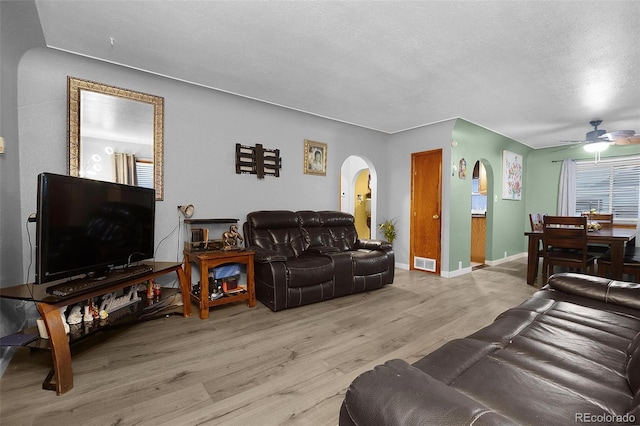 living area featuring arched walkways, visible vents, a textured ceiling, light wood-type flooring, and baseboards