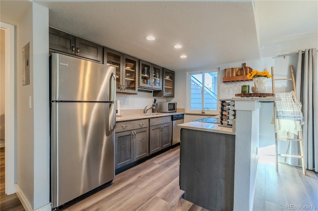 kitchen with stainless steel appliances, light stone counters, a kitchen breakfast bar, a textured ceiling, and light hardwood / wood-style flooring