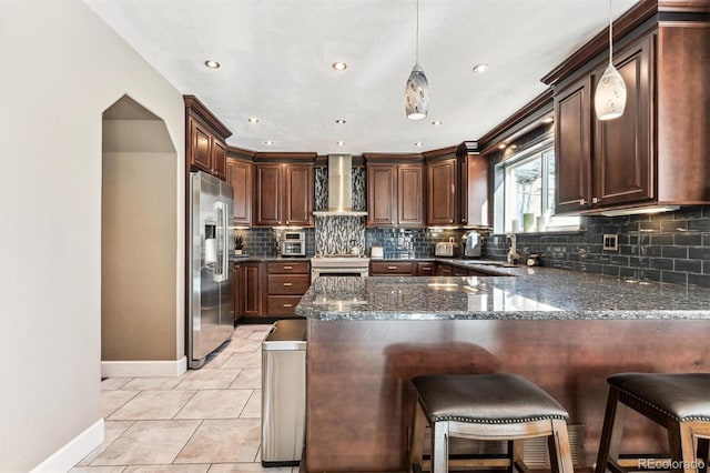 kitchen featuring a peninsula, wall chimney range hood, tasteful backsplash, and stainless steel appliances