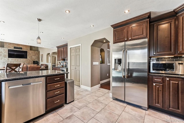 kitchen featuring arched walkways, decorative backsplash, appliances with stainless steel finishes, dark stone countertops, and dark brown cabinets