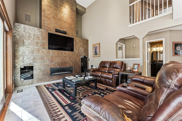 living area with a tile fireplace, a towering ceiling, and tile patterned floors