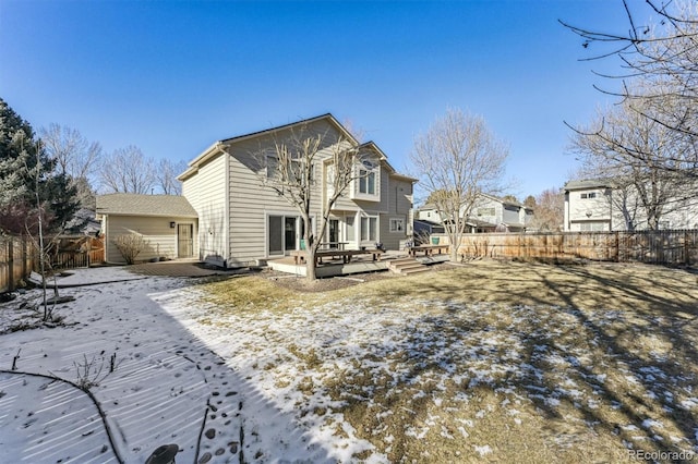 snow covered rear of property featuring a deck and a fenced backyard