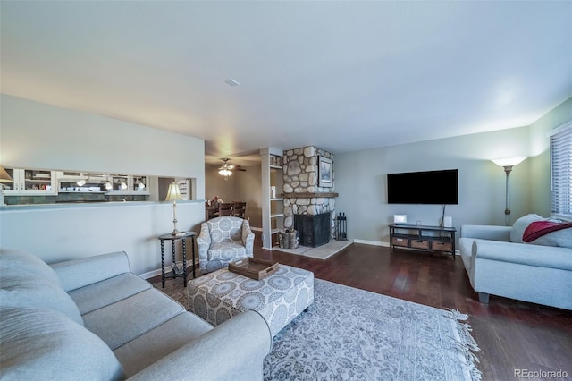 living room featuring ceiling fan, a stone fireplace, and dark hardwood / wood-style flooring