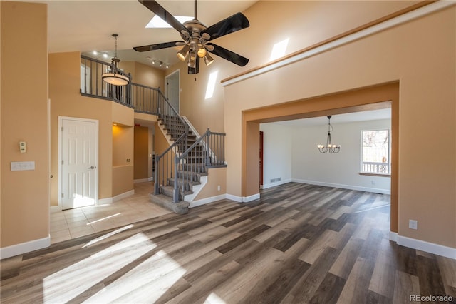 unfurnished living room featuring a towering ceiling, ceiling fan with notable chandelier, and hardwood / wood-style flooring