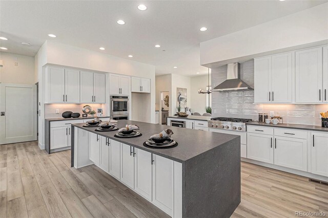 kitchen featuring light wood-type flooring, stainless steel appliances, white cabinetry, and wall chimney exhaust hood