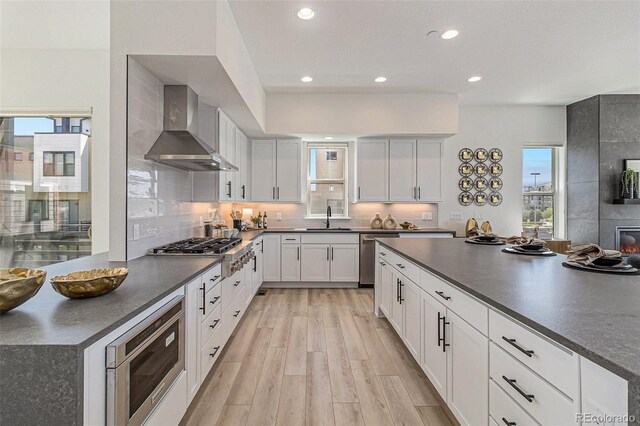 kitchen with white cabinets, light wood-type flooring, stainless steel appliances, and wall chimney range hood