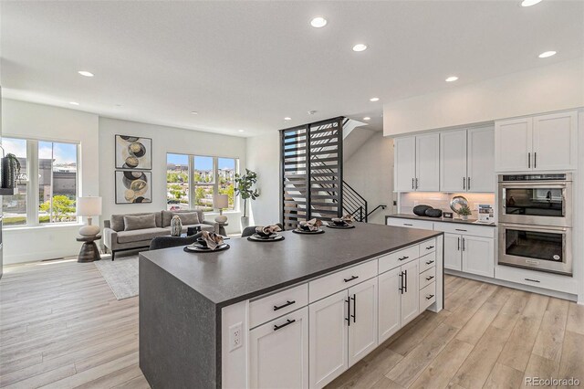 kitchen with double oven, white cabinets, and light wood-type flooring