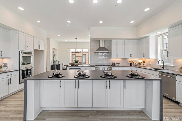 kitchen featuring sink, wall chimney exhaust hood, a kitchen island, and appliances with stainless steel finishes