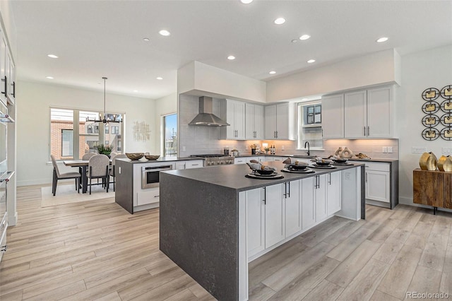 kitchen with decorative light fixtures, a kitchen island, light wood-type flooring, and wall chimney range hood