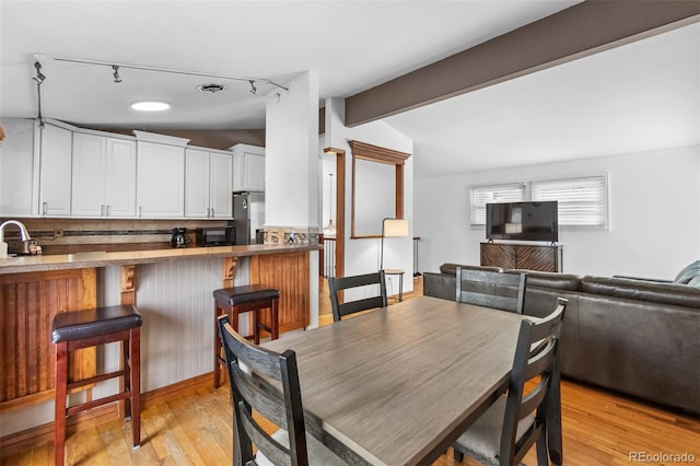 dining room featuring rail lighting, sink, light hardwood / wood-style flooring, and vaulted ceiling with beams