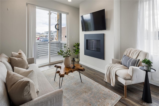 living room featuring a glass covered fireplace, recessed lighting, baseboards, and wood finished floors