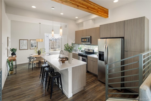 kitchen featuring an island with sink, a breakfast bar area, stainless steel appliances, and dark wood-style flooring