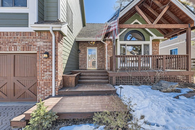 snow covered property entrance with brick siding and a garage