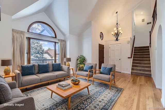 living room featuring high vaulted ceiling, light wood-style floors, baseboards, a chandelier, and stairs