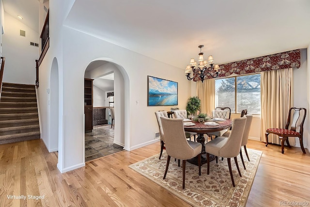 dining space featuring light wood-type flooring, a notable chandelier, stairway, arched walkways, and baseboards