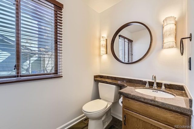 half bathroom featuring baseboards, toilet, and vanity