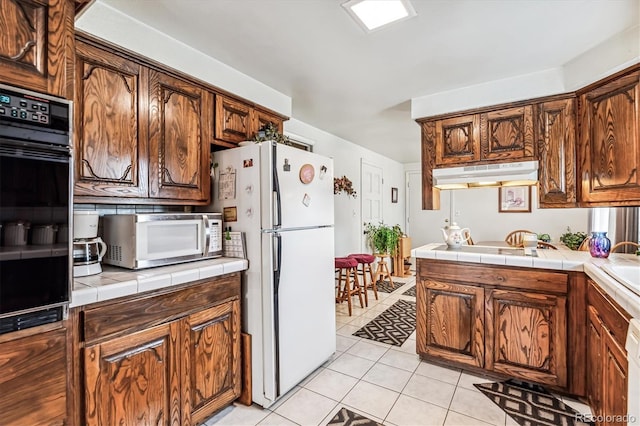 kitchen with light tile patterned floors, white appliances, and tile countertops