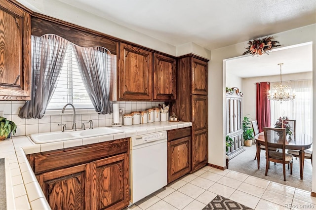 kitchen with dishwasher, sink, tasteful backsplash, tile countertops, and a chandelier