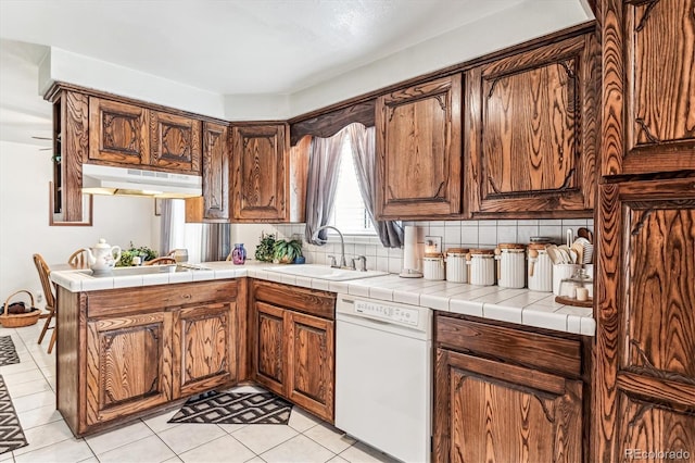 kitchen with tile counters, dishwasher, sink, backsplash, and kitchen peninsula