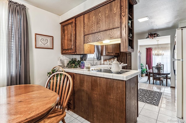 kitchen featuring tile countertops, an inviting chandelier, decorative backsplash, a textured ceiling, and white fridge