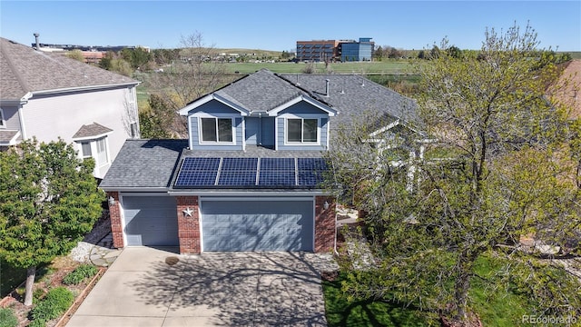 view of front facade featuring brick siding, concrete driveway, roof with shingles, and solar panels