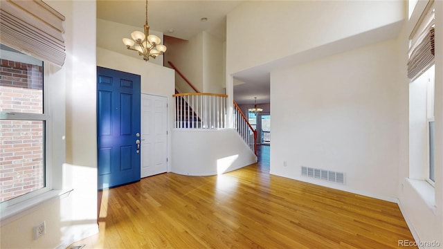 foyer featuring a high ceiling, a chandelier, light wood-style flooring, stairs, and visible vents