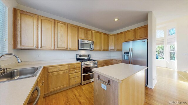 kitchen featuring appliances with stainless steel finishes, a sink, light wood finished floors, and a center island