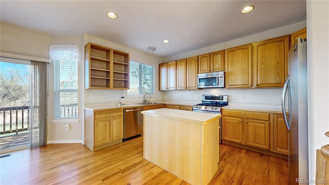 kitchen featuring appliances with stainless steel finishes, a sink, light countertops, light wood-type flooring, and a kitchen island