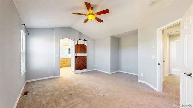interior space featuring a ceiling fan, visible vents, vaulted ceiling, a barn door, and light carpet