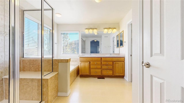 bathroom featuring double vanity, a shower stall, a garden tub, and a sink