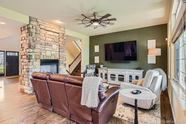 living room featuring a ceiling fan, wood finished floors, stairway, and a stone fireplace