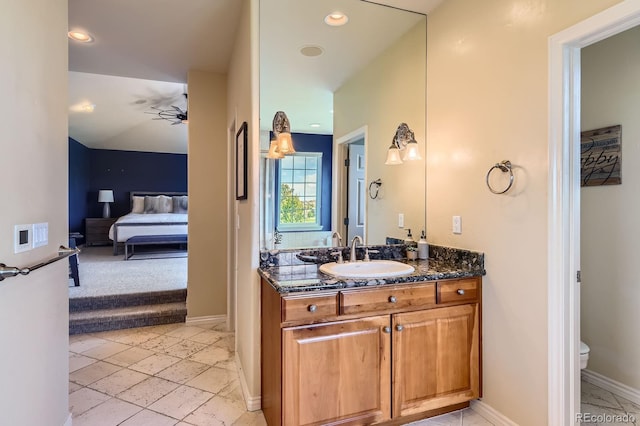 bathroom with ensuite bathroom, vanity, toilet, a ceiling fan, and baseboards