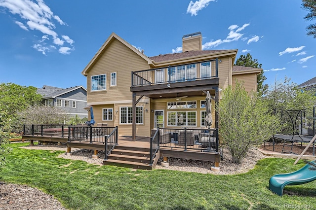 rear view of house with a balcony, a lawn, a chimney, and a playground