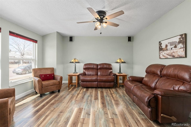 living room with a textured ceiling, ceiling fan, light wood finished floors, and baseboards