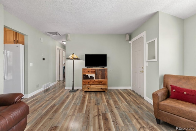 living room featuring a textured ceiling, wood finished floors, visible vents, and baseboards