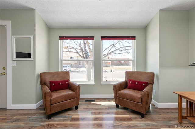 sitting room with visible vents, a textured ceiling, baseboards, and wood finished floors