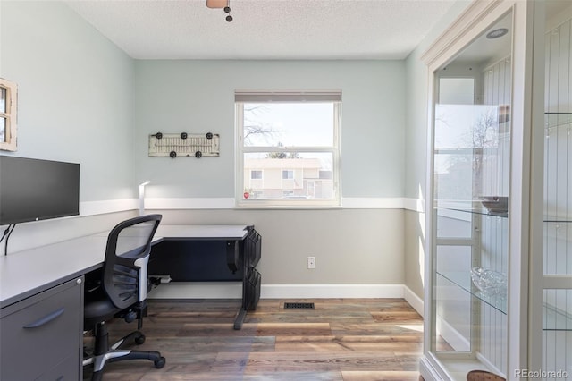 home office featuring baseboards, a textured ceiling, visible vents, and wood finished floors