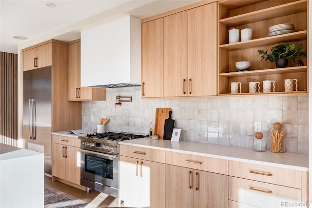 kitchen with decorative backsplash, appliances with stainless steel finishes, light brown cabinets, and wall chimney range hood