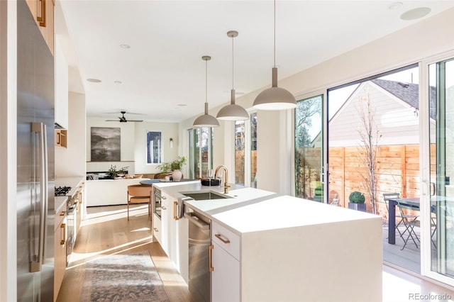 kitchen featuring sink, stainless steel appliances, hanging light fixtures, a kitchen island with sink, and white cabinets