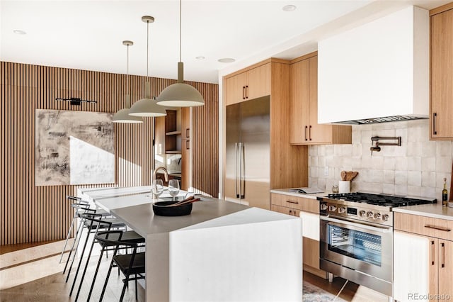 kitchen with an island with sink, appliances with stainless steel finishes, a breakfast bar, hanging light fixtures, and light countertops