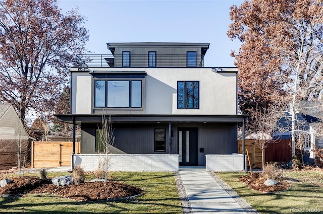 contemporary house with a front yard, fence, a balcony, and stucco siding