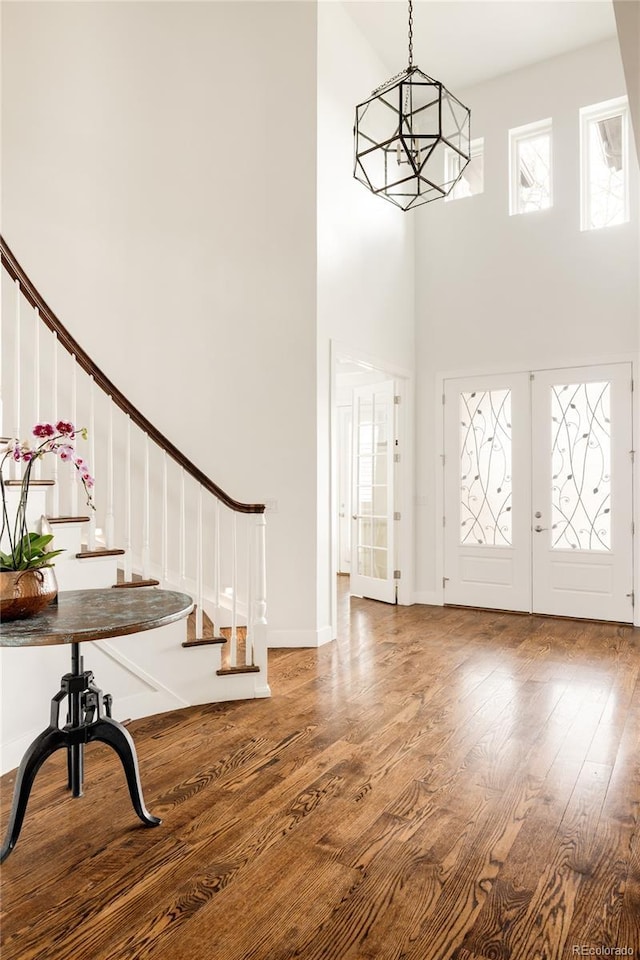 foyer entrance with a notable chandelier, wood finished floors, french doors, a towering ceiling, and stairs