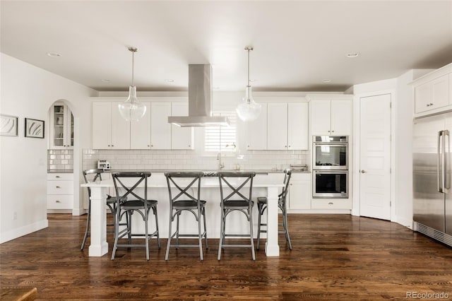 kitchen with a breakfast bar area, a center island, appliances with stainless steel finishes, and island range hood