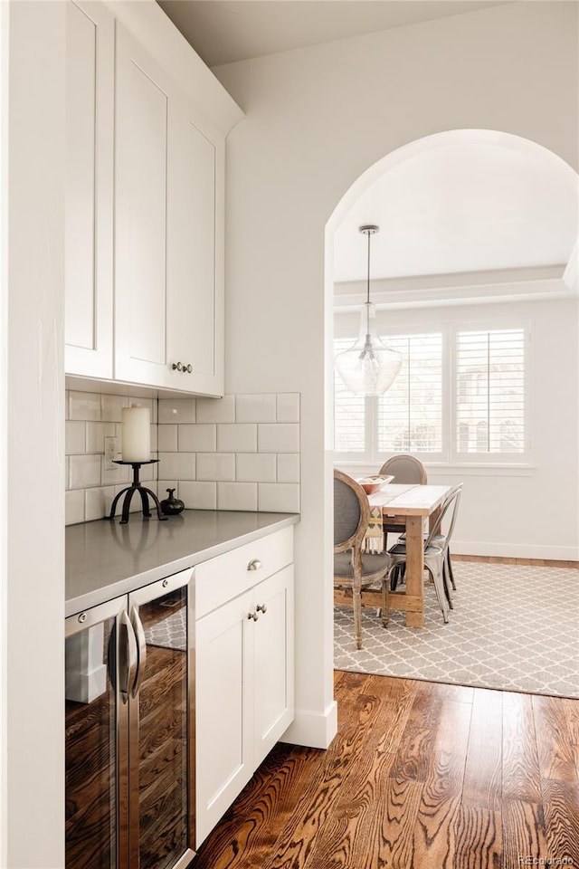 kitchen with dark wood-type flooring, wine cooler, decorative backsplash, arched walkways, and white cabinets